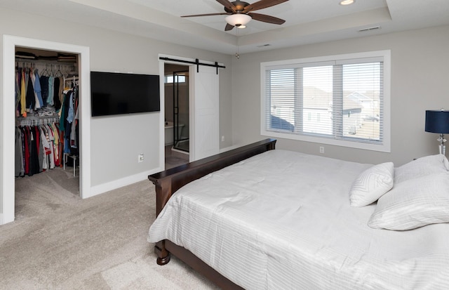 carpeted bedroom with a barn door, a spacious closet, ceiling fan, and a tray ceiling