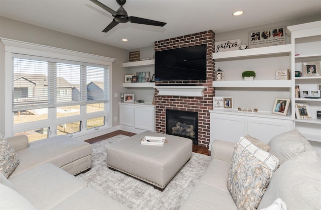 living room featuring ceiling fan, a brick fireplace, and light wood-type flooring