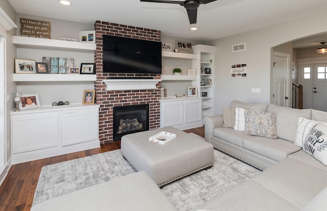 living room featuring dark wood-type flooring, ceiling fan, and a brick fireplace