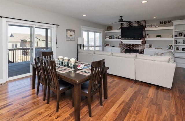 dining space featuring ceiling fan, dark hardwood / wood-style flooring, and a brick fireplace