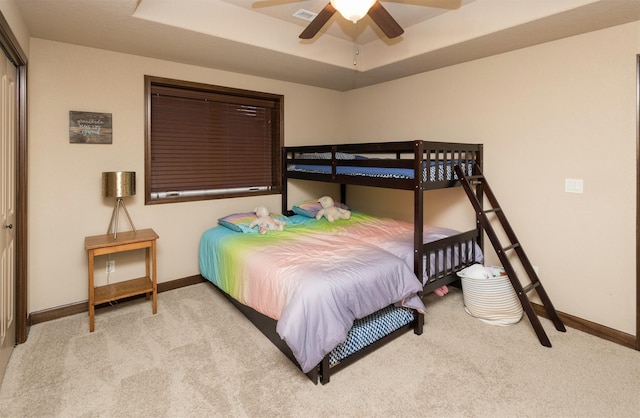 carpeted bedroom with a closet, a raised ceiling, and ceiling fan