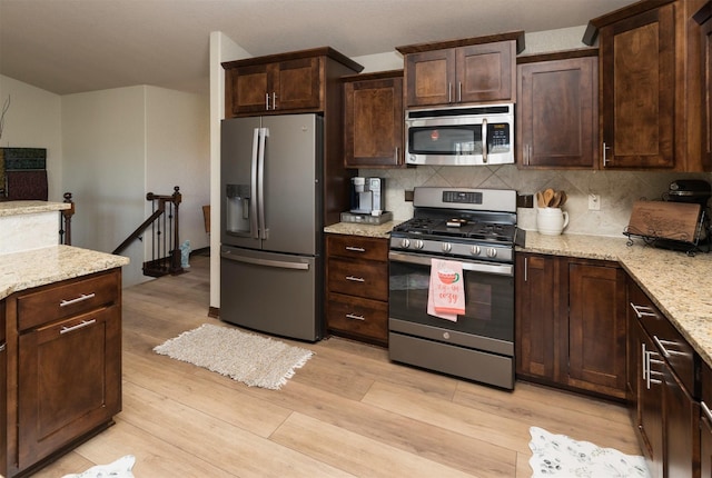 kitchen featuring tasteful backsplash, dark brown cabinets, light hardwood / wood-style flooring, appliances with stainless steel finishes, and light stone countertops