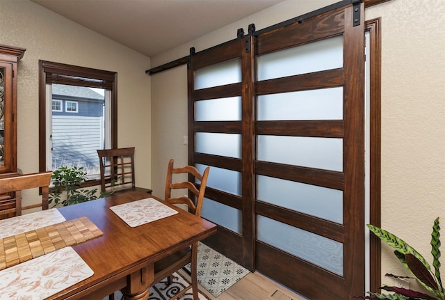 dining room with light hardwood / wood-style flooring, vaulted ceiling, and a barn door