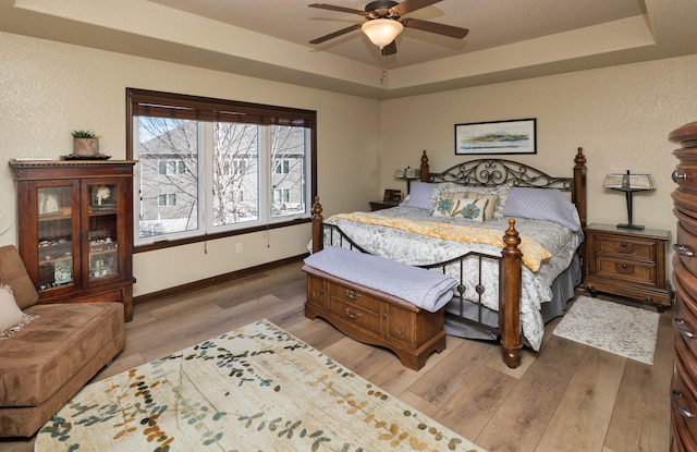 bedroom with a raised ceiling, hardwood / wood-style flooring, and ceiling fan