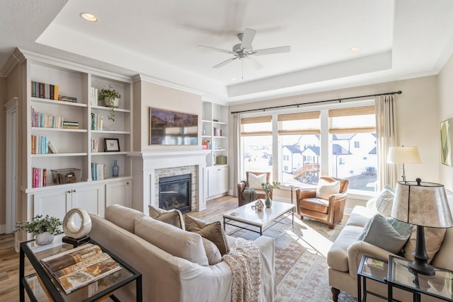 living room featuring built in shelves, a tray ceiling, a tile fireplace, and light hardwood / wood-style flooring