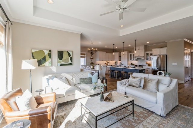 living room featuring plenty of natural light, a raised ceiling, ceiling fan with notable chandelier, and light wood-type flooring