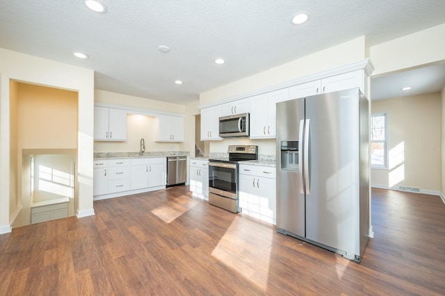 kitchen with dark hardwood / wood-style floors, white cabinetry, stainless steel appliances, light stone countertops, and a textured ceiling