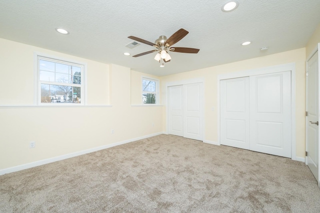 unfurnished bedroom with multiple closets, light colored carpet, a textured ceiling, and ceiling fan