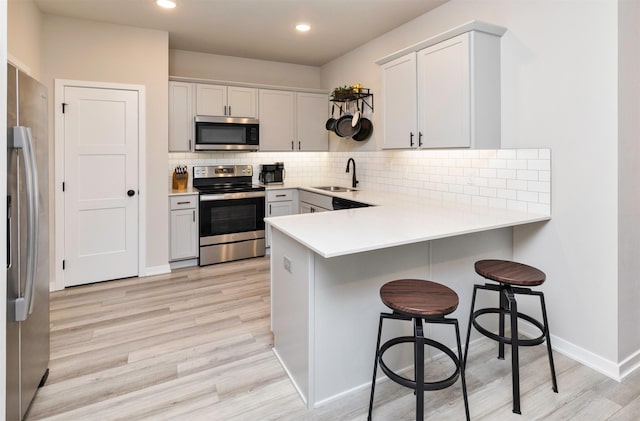 kitchen featuring appliances with stainless steel finishes, a breakfast bar, sink, white cabinets, and kitchen peninsula