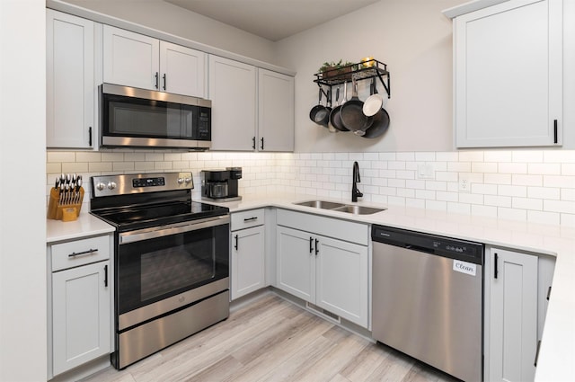 kitchen with stainless steel appliances, sink, light wood-type flooring, and decorative backsplash