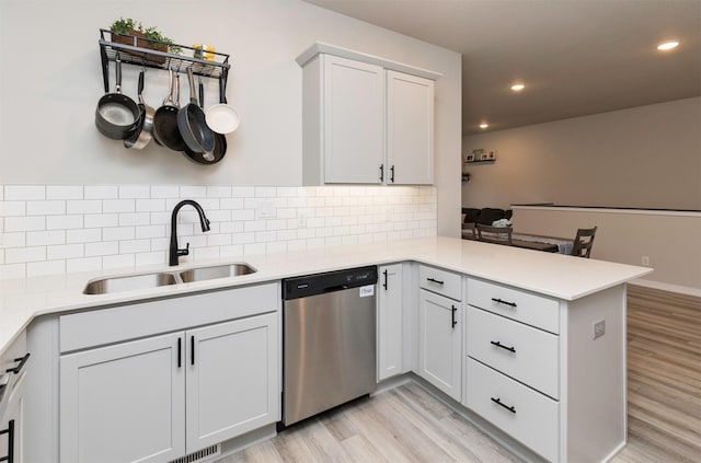 kitchen with sink, light hardwood / wood-style flooring, dishwasher, kitchen peninsula, and white cabinets