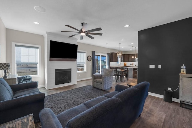 living room featuring dark wood-type flooring, a large fireplace, and ceiling fan