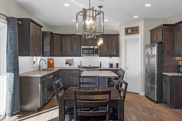 kitchen featuring dark brown cabinetry, sink, light stone counters, appliances with stainless steel finishes, and pendant lighting