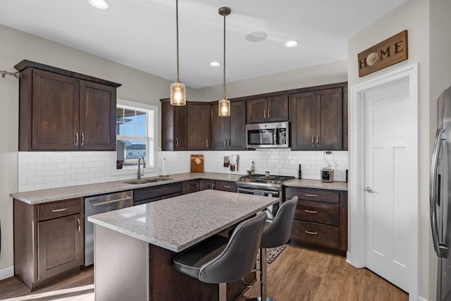 kitchen featuring sink, decorative light fixtures, a center island, appliances with stainless steel finishes, and light stone countertops