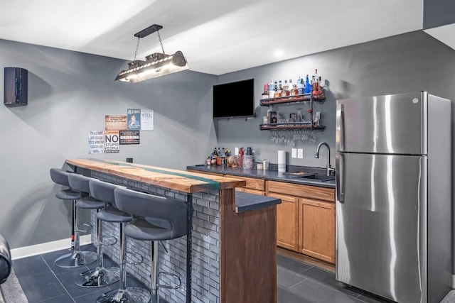 bar featuring sink, decorative light fixtures, stainless steel refrigerator, and dark tile patterned flooring