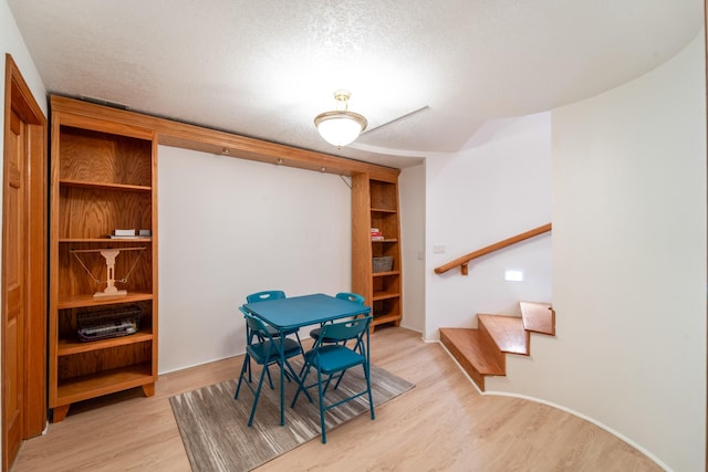 dining area with light wood-style floors, stairs, and a textured ceiling