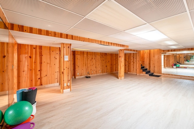 finished below grade area featuring stairway, wood finished floors, a paneled ceiling, and wooden walls