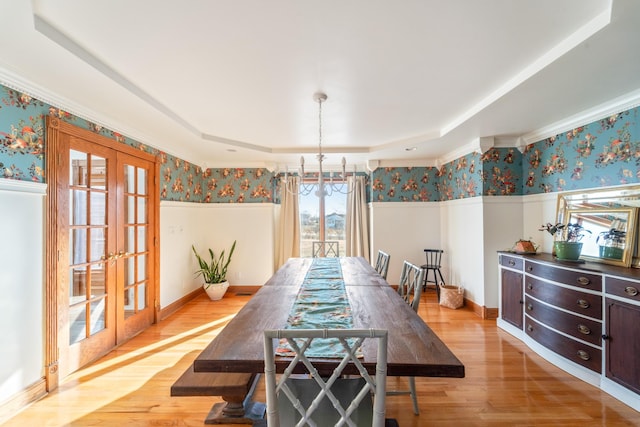 dining space with wallpapered walls, a raised ceiling, wainscoting, light wood-style flooring, and french doors