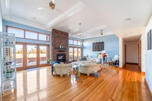 living room with a brick fireplace, ceiling fan, light wood finished floors, and beamed ceiling