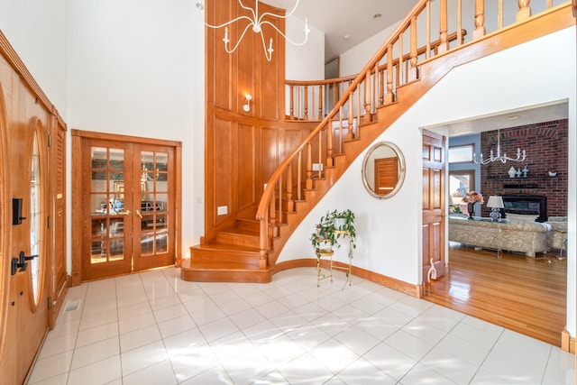 stairs with a towering ceiling, a brick fireplace, baseboards, and tile patterned floors