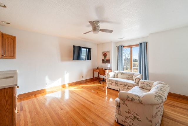 living area with light wood-style flooring, baseboards, and a textured ceiling