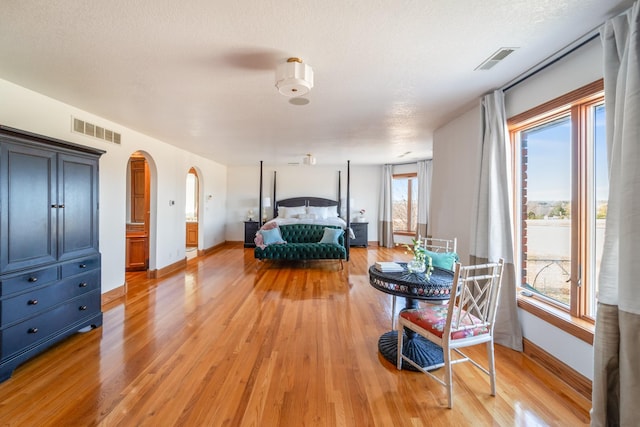 bedroom featuring light wood-style flooring, visible vents, and arched walkways