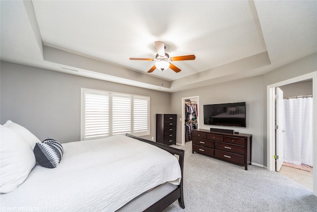 carpeted bedroom featuring a closet, a walk in closet, ceiling fan, and a tray ceiling