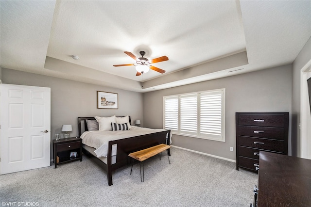 bedroom featuring light carpet, a tray ceiling, and ceiling fan