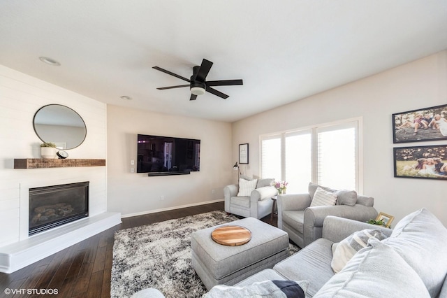 living room featuring ceiling fan, a large fireplace, and dark hardwood / wood-style floors