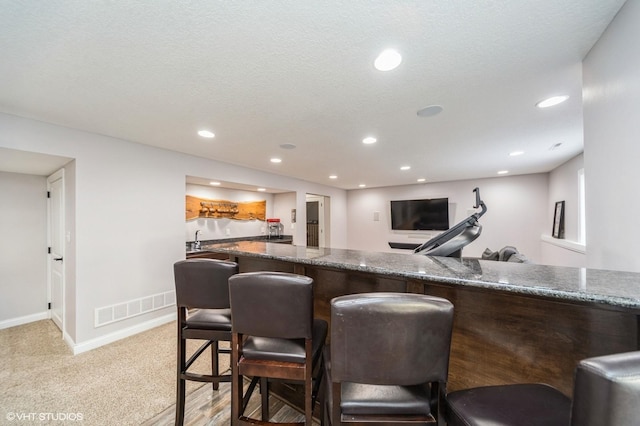 bar with sink, light colored carpet, a textured ceiling, and dark stone counters