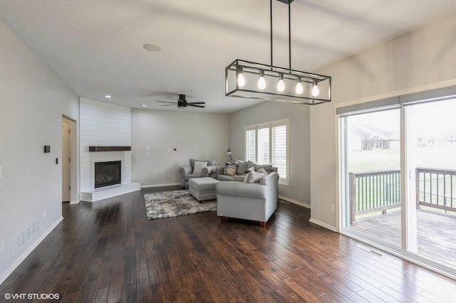 living room with a large fireplace, dark wood finished floors, baseboards, and ceiling fan