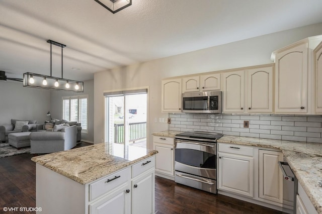 kitchen featuring tasteful backsplash, open floor plan, decorative light fixtures, dark wood finished floors, and appliances with stainless steel finishes