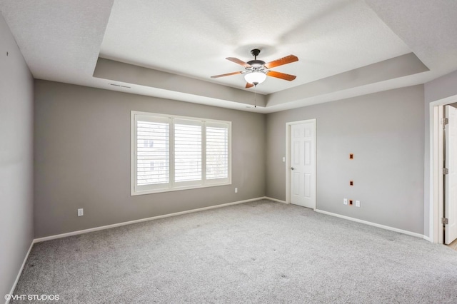 carpeted spare room with a textured ceiling, baseboards, a ceiling fan, and a raised ceiling