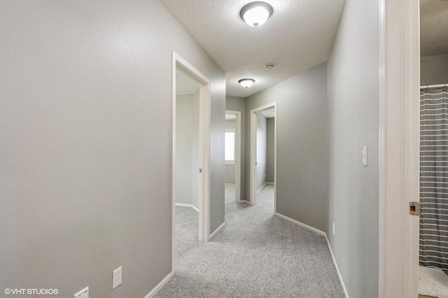 hallway featuring carpet floors, baseboards, and a textured ceiling