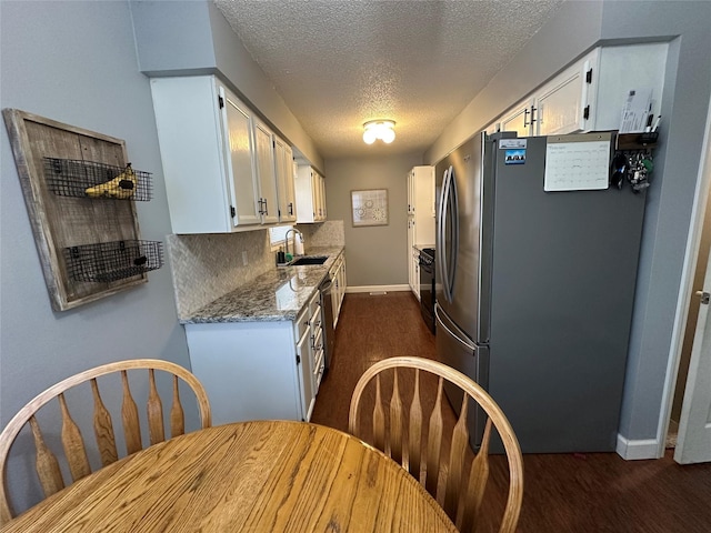 kitchen featuring stainless steel refrigerator, sink, backsplash, white cabinets, and light stone counters