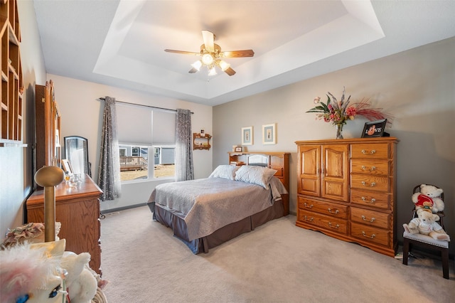 bedroom with light colored carpet, a raised ceiling, and ceiling fan