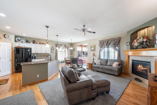 living room featuring a tiled fireplace, ceiling fan, sink, and light wood-type flooring