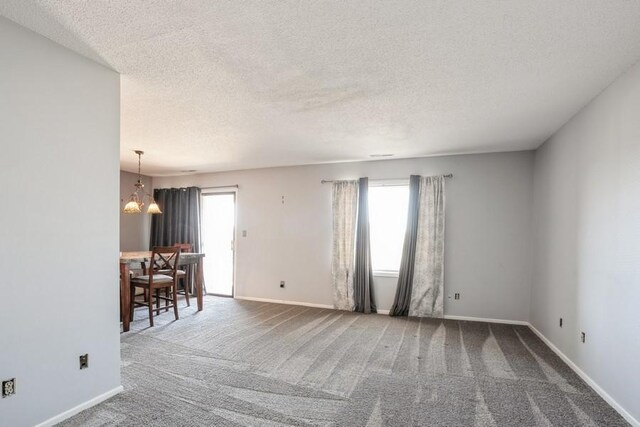 carpeted spare room with an inviting chandelier and a textured ceiling