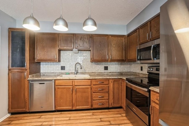 kitchen featuring stainless steel appliances, light wood-style floors, a sink, and decorative backsplash