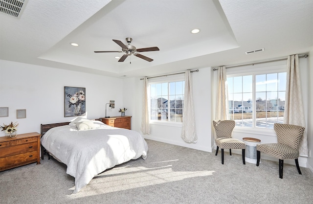 carpeted bedroom with a ceiling fan, a tray ceiling, baseboards, and visible vents