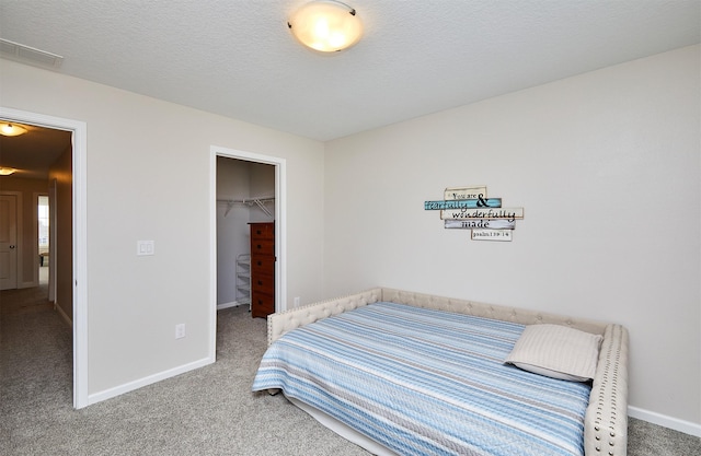 bedroom featuring a spacious closet, carpet, baseboards, and a textured ceiling