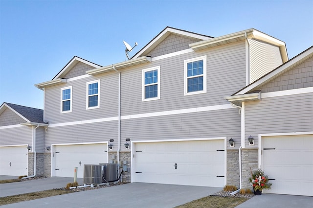 view of property with a garage, stone siding, and central AC unit