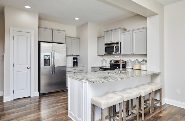 kitchen featuring gray cabinetry, light stone counters, tasteful backsplash, appliances with stainless steel finishes, and dark wood-style flooring