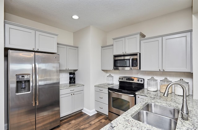 kitchen with tasteful backsplash, light stone countertops, dark wood-style floors, stainless steel appliances, and a sink