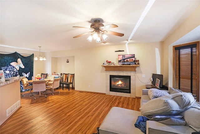 living room featuring ceiling fan with notable chandelier, hardwood / wood-style floors, and a tile fireplace