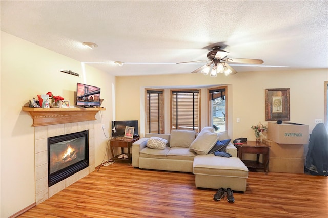 living room with ceiling fan, wood-type flooring, a tile fireplace, and a textured ceiling