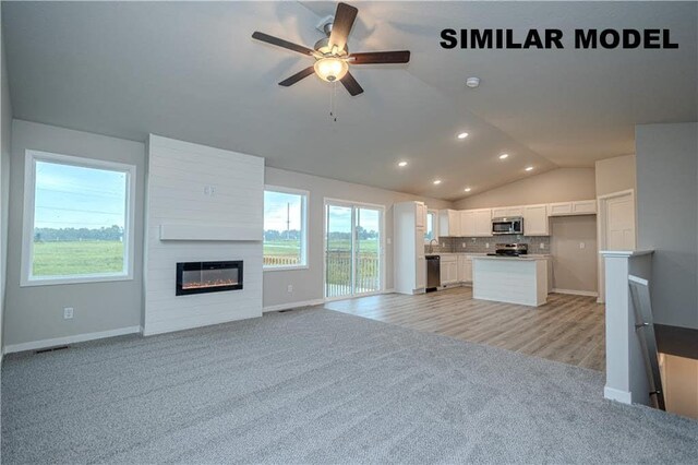 kitchen with ceiling fan, stainless steel appliances, a fireplace, light carpet, and vaulted ceiling