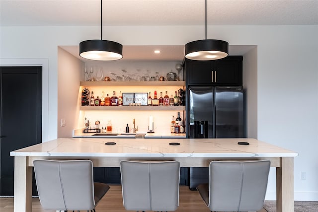 bar with a textured ceiling, hanging light fixtures, black refrigerator with ice dispenser, and wet bar