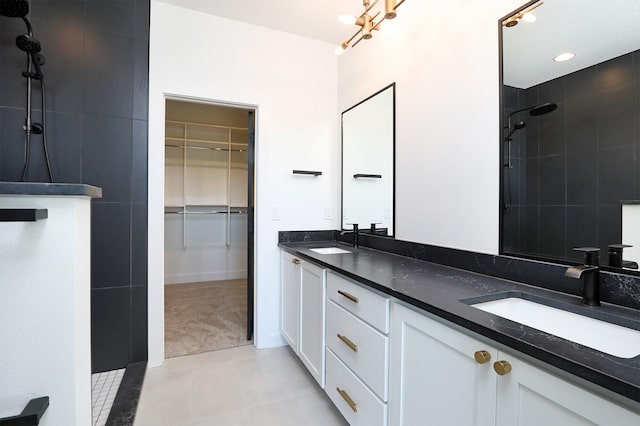 full bath with double vanity, a spacious closet, a sink, and tiled shower