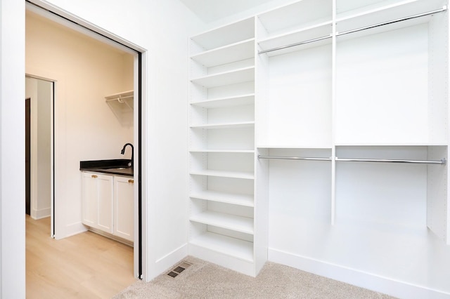 spacious closet featuring light colored carpet, a sink, and visible vents